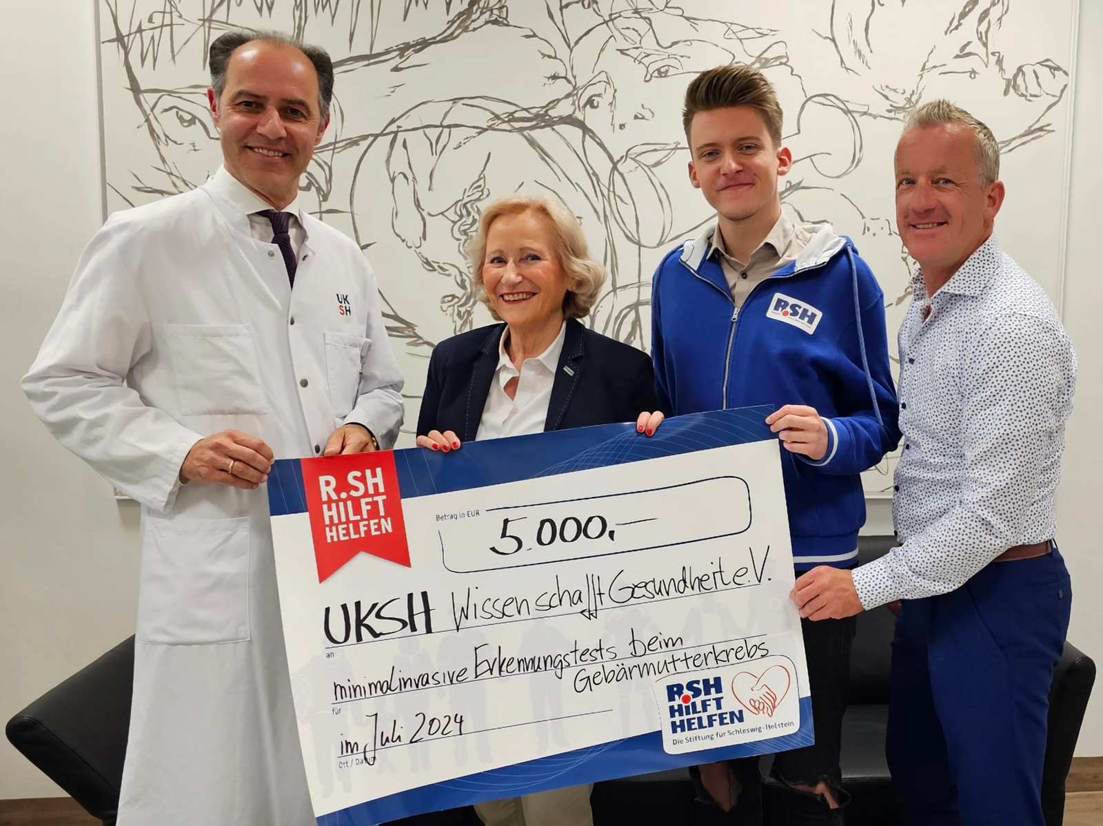 Drei Männer und eine Frau stehen hinter einem Spendencheck und lächeln in die Kamera